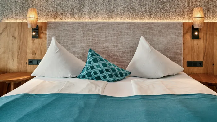 Modernes Hotelzimmerbett mit türkiser Bettdecke und Zierkissen